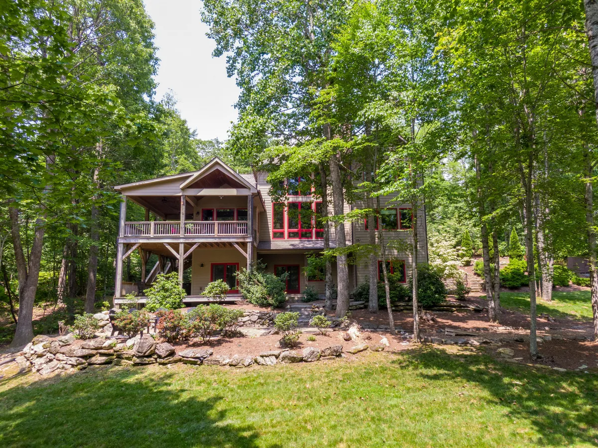 A spacious wooden deck surrounded by lush greenery, bright red window frames, and stone landscaping. The deck is set up for gatherings, barbecues, or quiet nature-inspired relaxation, blending seamlessly into the natural mountain environment.