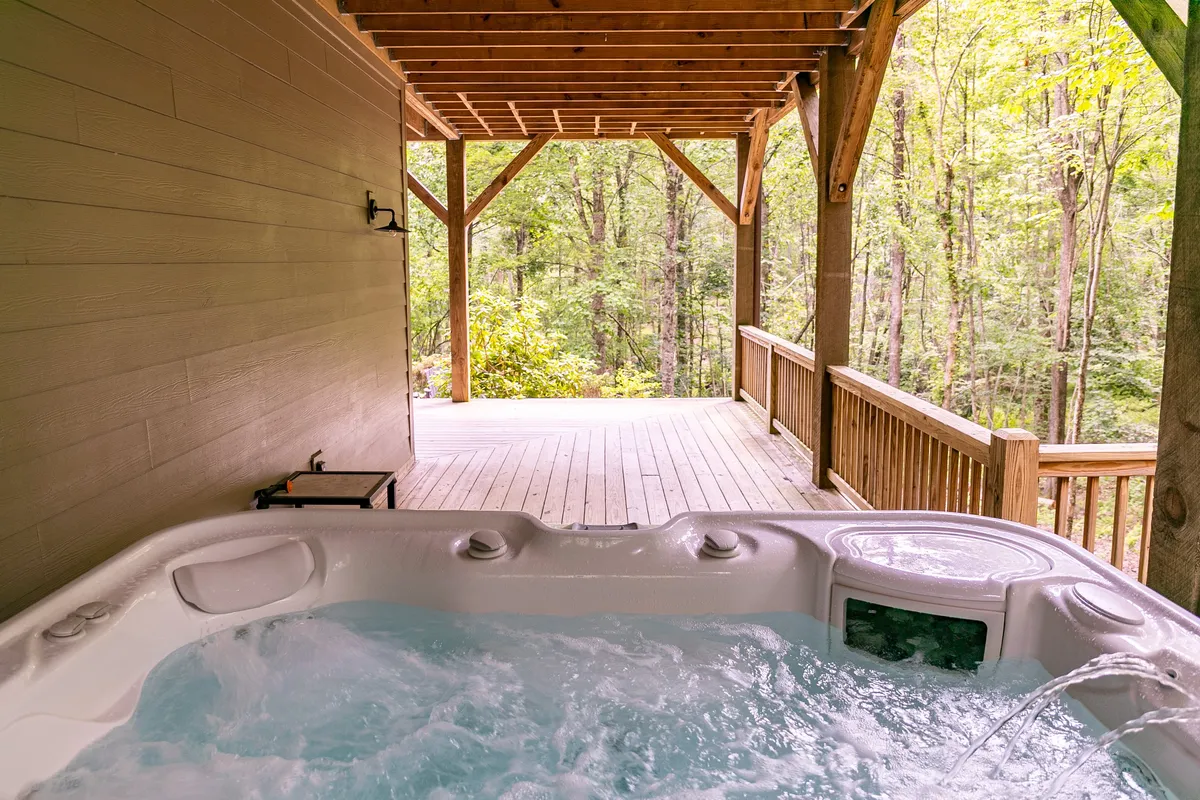 An inviting exterior deck with a large hot tub surrounded by wooden decking and trees, offering a serene spot for relaxation, soaking, and social gatherings while immersed in nature.