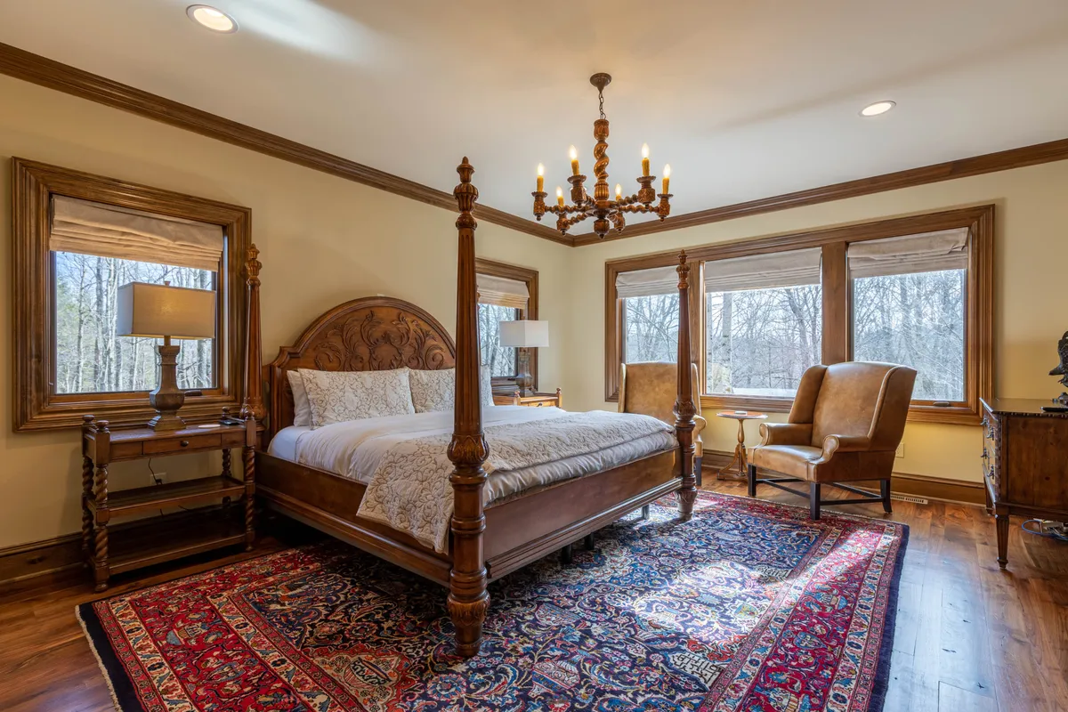 A serene bedroom featuring a four-poster bed, chandelier, large windows letting in natural light, antique furniture, and a cozy rug. The atmosphere feels comforting and elegant, with soft morning light and tranquil decor.