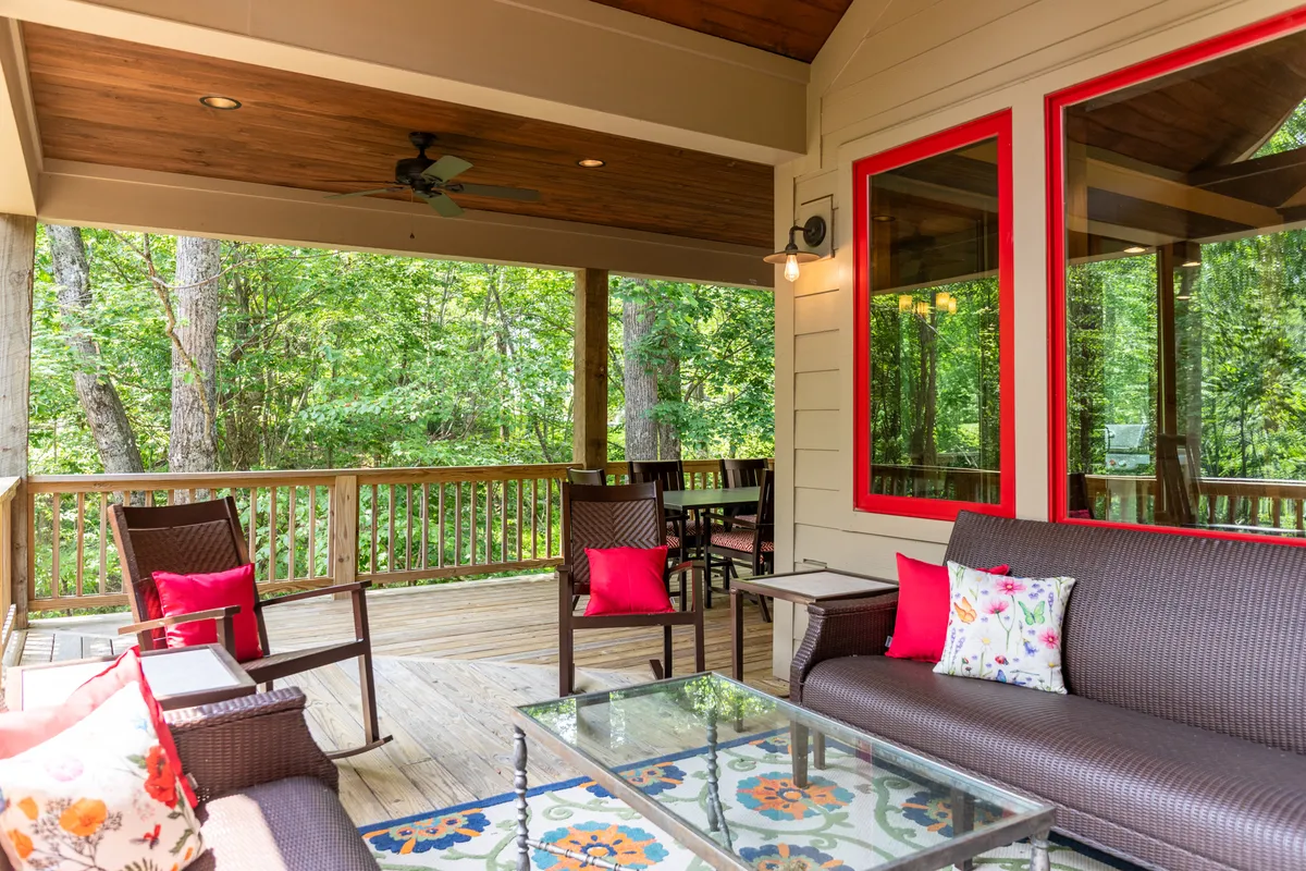 A comfortable outdoor seating area on a wooden deck, accented by colorful pillows, overlooks lush greenery. The space invites relaxation and is accessible directly from the main living areas, blurring the line between indoor and outdoor communal living.