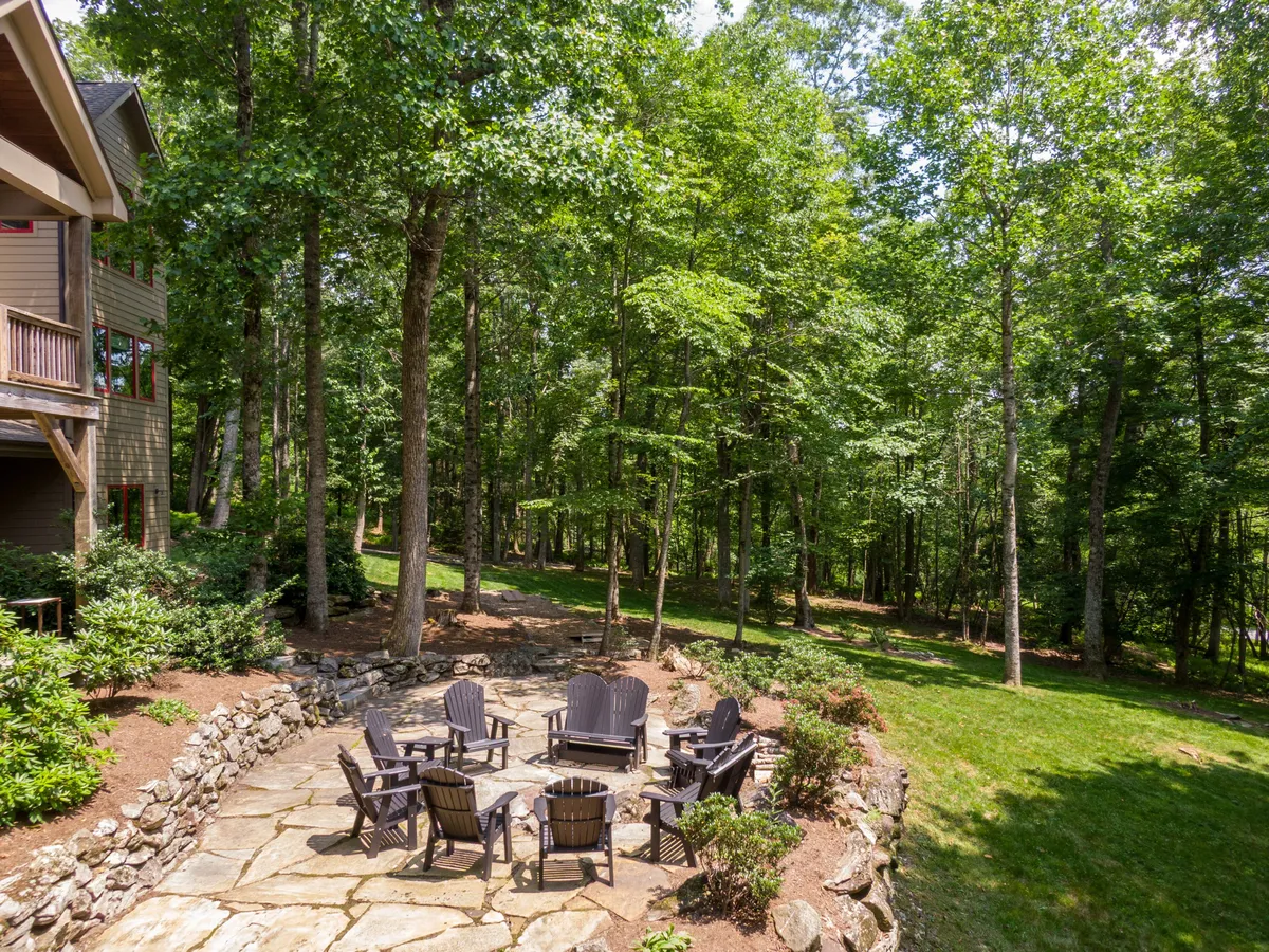 A cozy stone fire pit surrounded by Adirondack chairs, set amidst lush greenery and a walking path, creating a welcoming space for outdoor gatherings and fireside evenings.