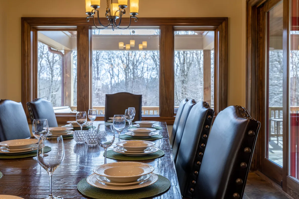 This image presents a long, elegant dining table under a chandelier, surrounded by dining chairs and bathed in natural light from large windows. The setting is ideal for both formal dinners and lively family game nights.