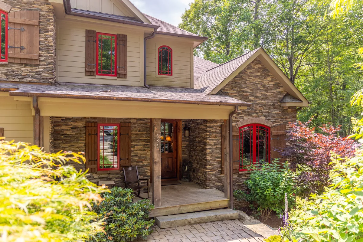 This image shows the welcoming front porch of the lodge, featuring a charming stone facade, red window trim, and wooden shutters. The inviting porch setting hints at relaxed evenings and the mountain home's architectural style.