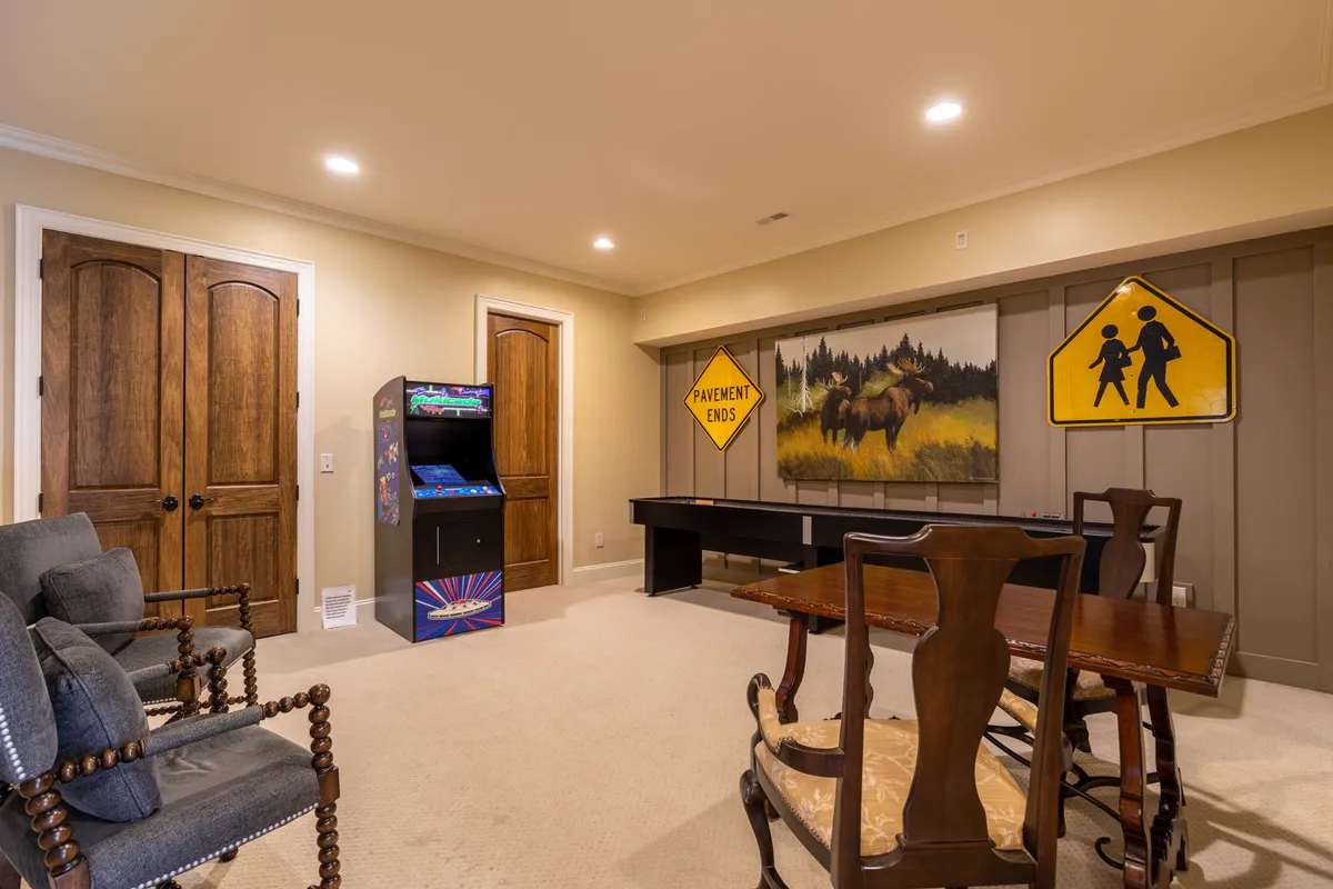 A bright, engaging area featuring a vintage arcade machine, a wooden dining table and chairs ideal for cards or board games, and quirky moose artwork with road signs, offering a fun, casual retreat for all ages.