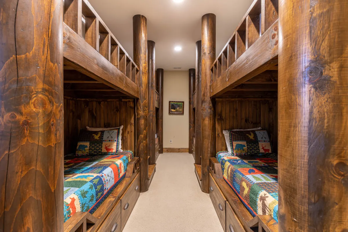 A playful lower-level bunkroom with custom bunk beds crafted from real tree trunks, colorful quilts adorning each bed, and framed artwork on the wall. The space feels warm, whimsical, and perfect for groups or families.